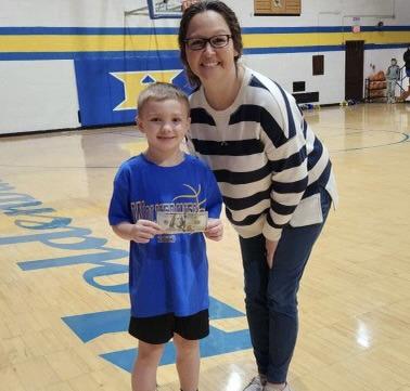 Mary Arthur from Security State Bank presents a hundred dollar bill to Raden Tillery after Raden sank a long shot at the intermission of the Wolverines game with Chandler. Security State Bank sponsors a contest to give a Wolverine fan an opportunity to sink a half-court shot for $100 at each Wolverine game.